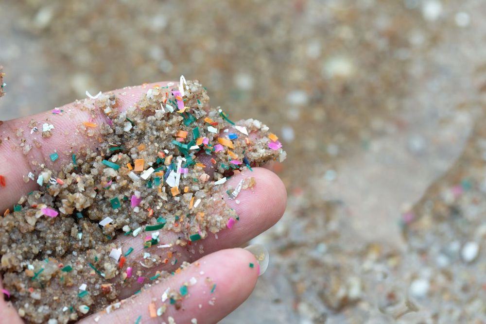 photo d'une main pleine de sable et de granulés de plastique