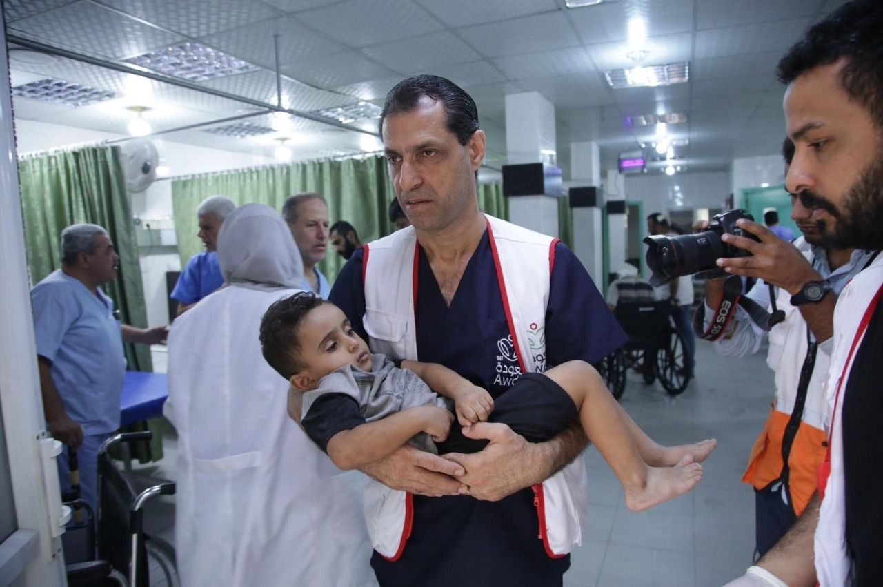 Foto van Dr Muhanna in een ziekenhuisgang met een gewond kind in zijn armen