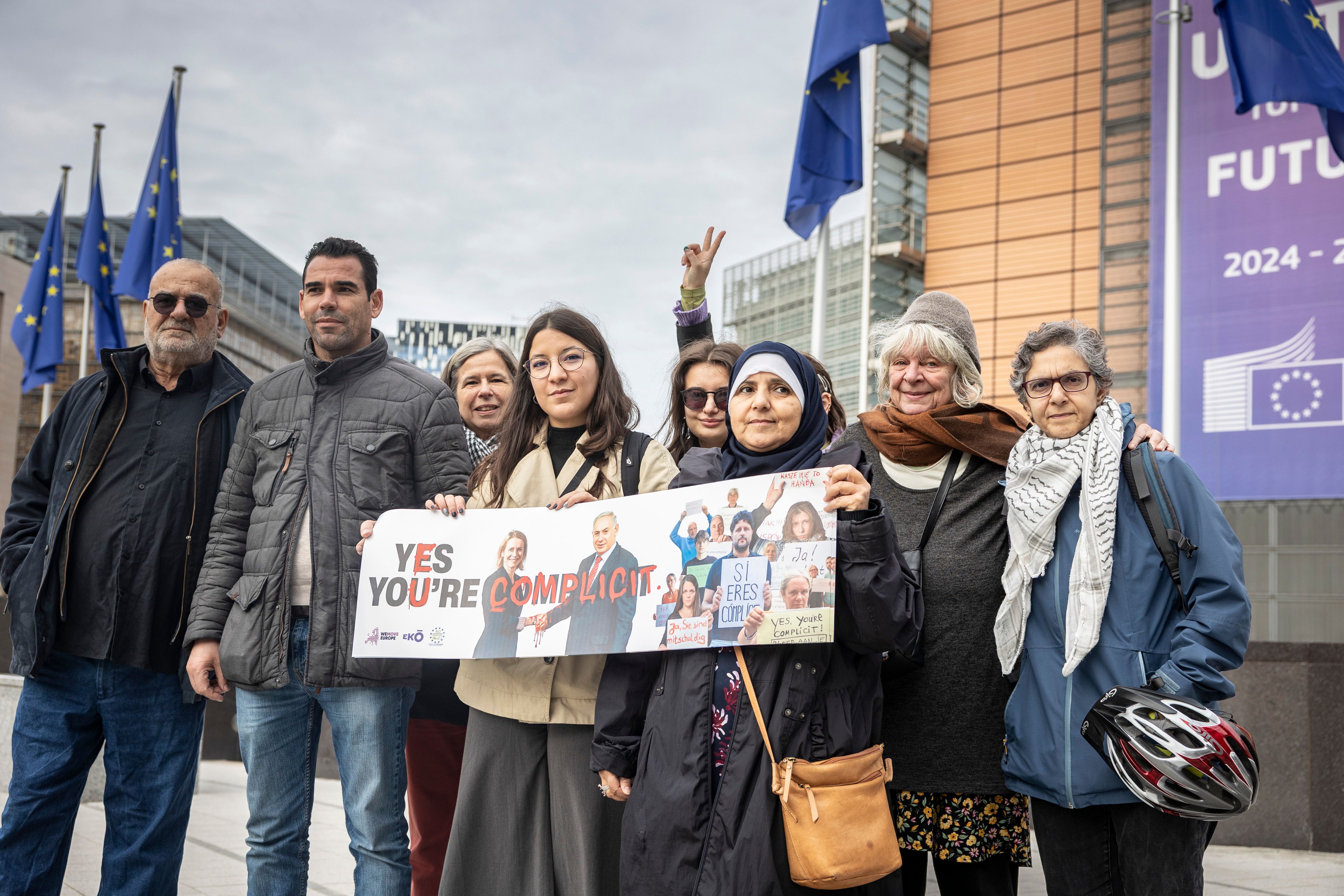 We hold a banner covered with photos and messages from this community, calling on the EU to end its complicity with Israel.