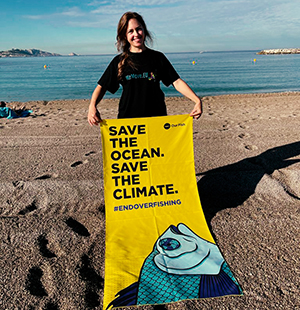 Mika, die Repräsentantin von WeMove, hält ein Handtuch mit der Aufschrift ,,Rettet den Ozean. Rettet das Klima.