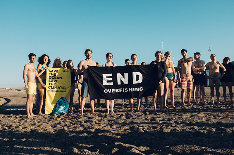 Die Teilnehmer stehen versammelt und halten ein Handtuch mit der Aufschrift 'Stoppt die Überfischung'