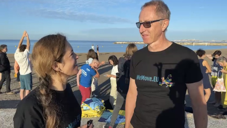 Mika, eine Koordinatorin von WeMove Europe, steht am Strand und spricht mit dem Segler Laurent über seine Erfahrungen.