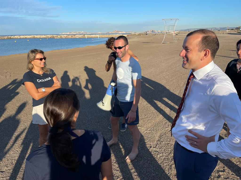 Der Kommissar Virginijus Sinkevičius steht im Anzug auf dem Strand und redet mit unseren Partnern von Oceana und Our Fish