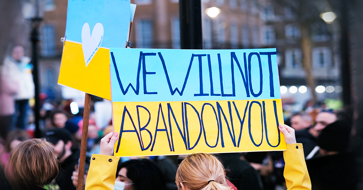 Photo von einer Frau, die ein blau gelbes Schild hochhält, auf dem steht: WE WILL NOT ABANDON YOU