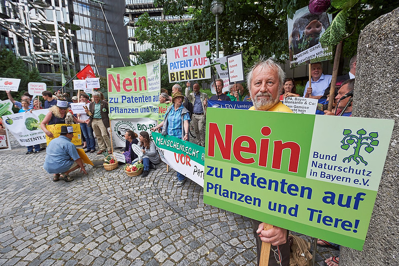 Man stands to right, holds red and green protest sign in front of group of protestors