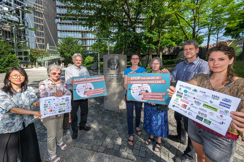 Seven people stand outside in semi-circle holding small placards