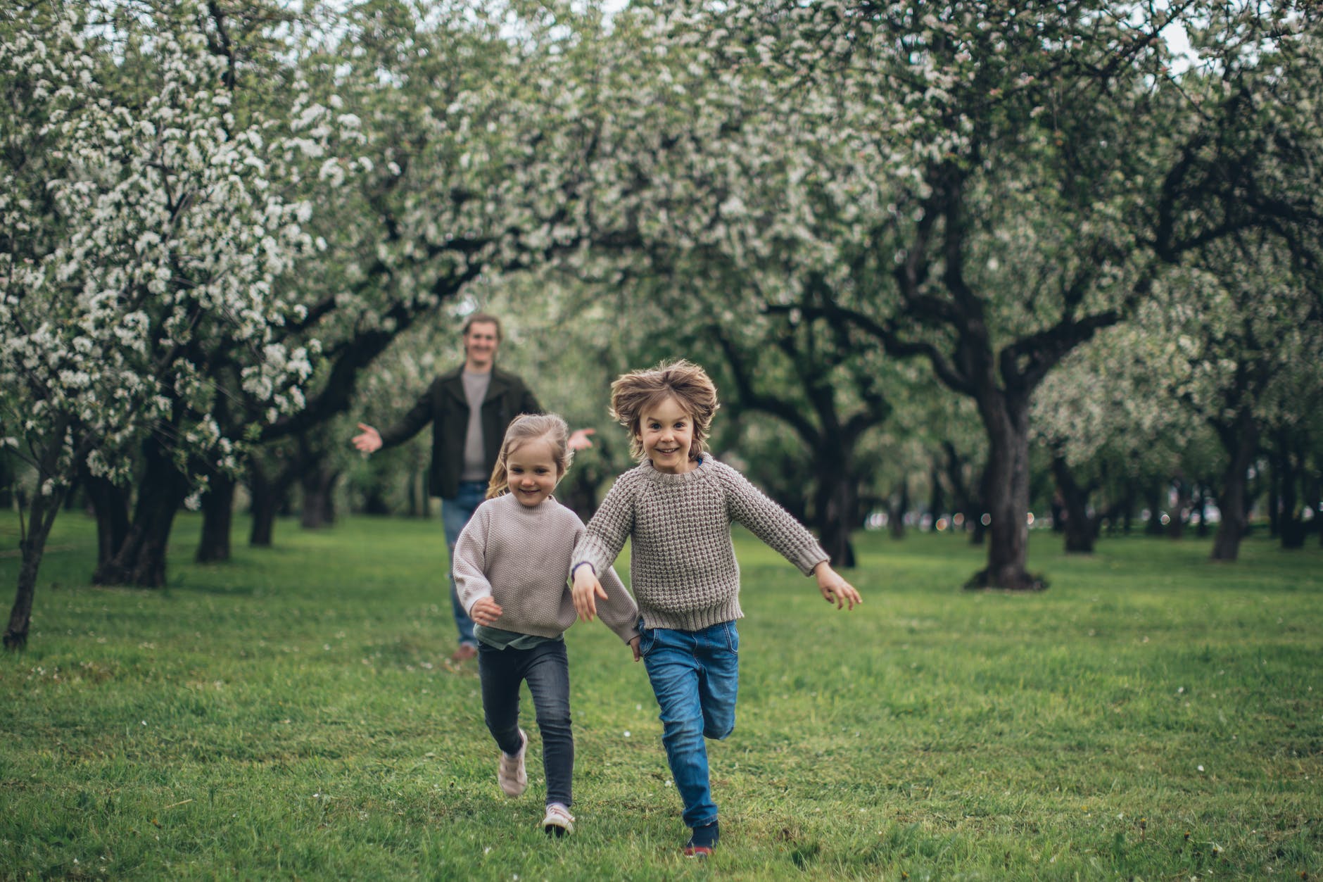 Zwei Kindern und ihr Vater rennen glücklich unter Obstbäumen entlang