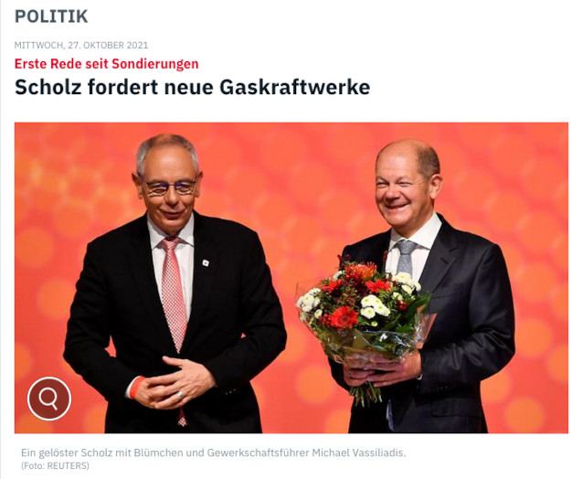 Zeitungsausschnitt, 27. Oktober 2021. Überschrift: Scholz fordert neue Gaskraftwerke. Darunter ein Photo: Ein gelöster Scholz mit Blümchen und Gewerkschaftsführer Vasiliadis